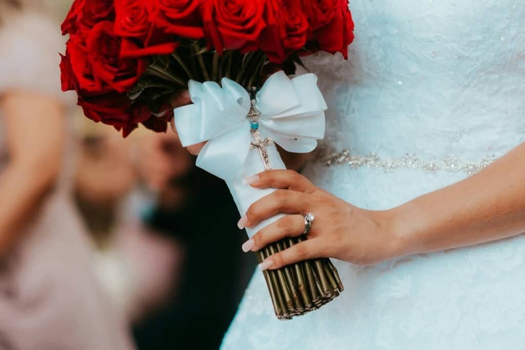 Close-up of a bride holding a red rose bouquet with wedding dress details.